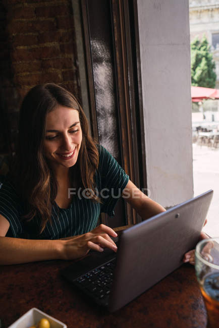 Ritratto di donna allegra che digita sul computer portatile nel caffè — Foto stock