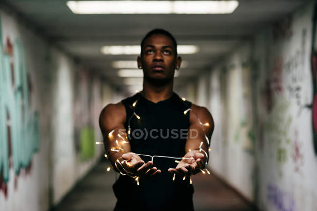 Man outstretching hands tied with lighten garland and looking up at underground passage — Stock Photo