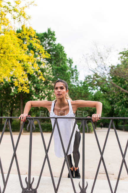 Спортивная девушка отжимается на заборе в парке — стоковое фото