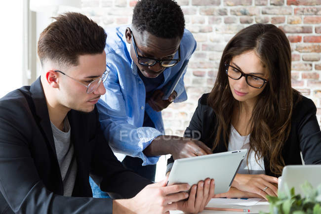 Portrait of multiethnic businesspeople using tablet at meeting in modern office. — Stock Photo