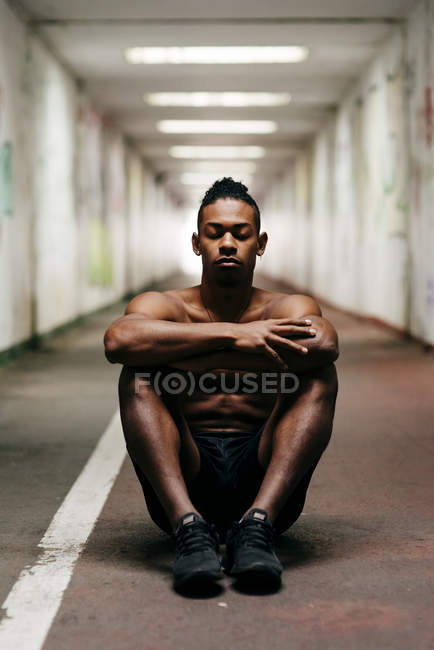 Shirtless sportsman sitting on floor with eyes closed at underground passage — Stock Photo