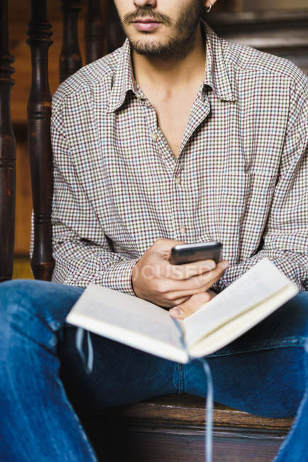 Mid section of man with notebook in hand and browsing smartphone — Stock Photo