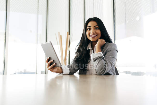 Portrait of businesswoman with tablet sitting at table and looking at camera — Stock Photo