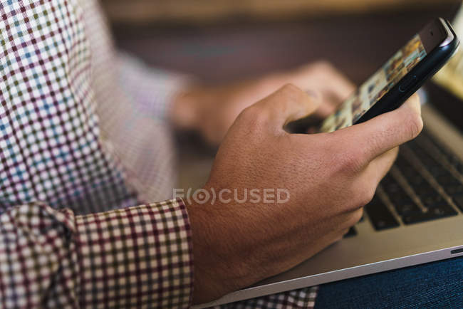 Männerhände mit Smartphone über Laptop auf Knien — Stockfoto