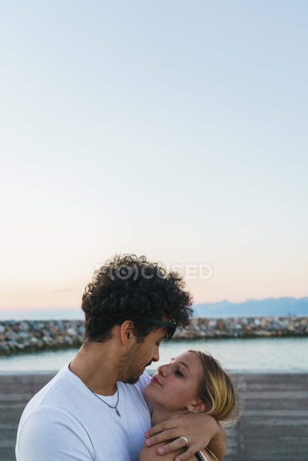 Seitenansicht eines sich umarmenden Paares, das jeden auf der Seebrücke ansieht — Stockfoto