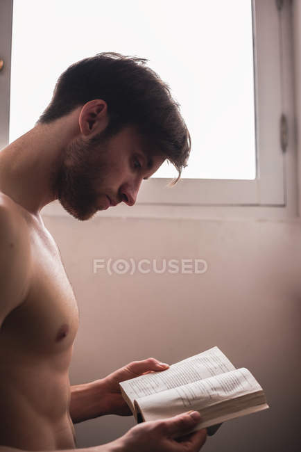 Junger Mann ohne Hemd liest Buch — Stockfoto