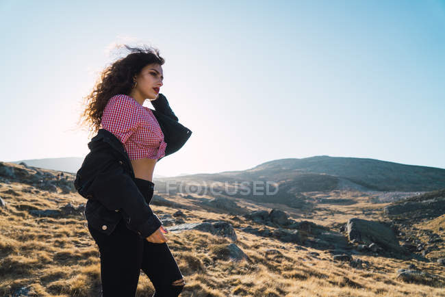 Vista lateral de mujer morena en camisa a cuadros caminando por el campo - foto de stock