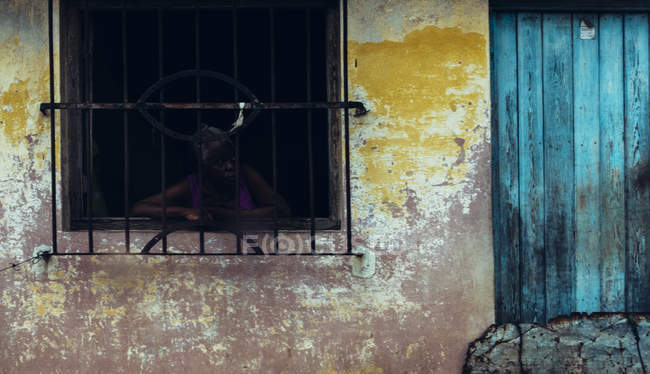 Kuba - 27. August 2016: Frau blickt aus dem Fenster hinter Gittern in altem schäbigen Haus. — Stockfoto