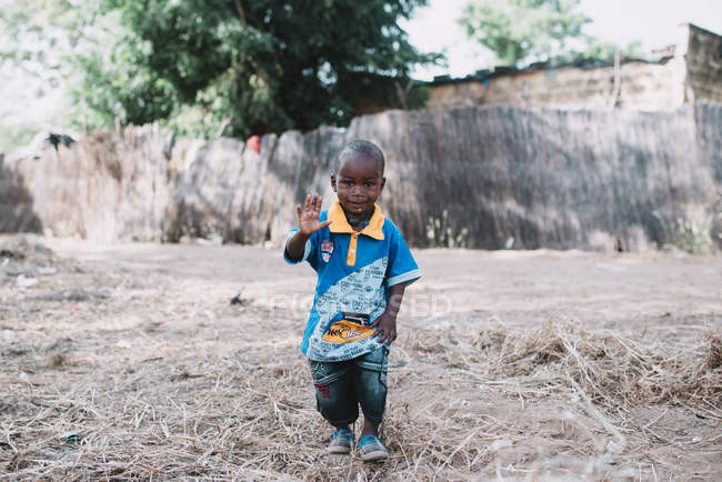 Goree, Senegal- diciembre 6, 2017: Un niño pequeño y adorable caminando por la calle rural y saludando a la cámara . - foto de stock