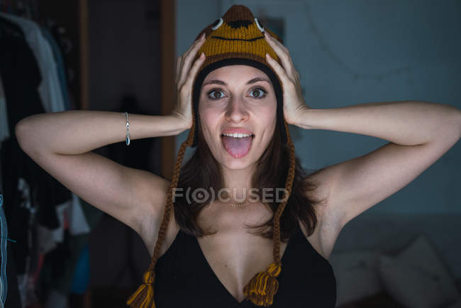 Brunette fille portant bonnet drôle tricoté et regardant la caméra avec bouche ouverte — Photo de stock