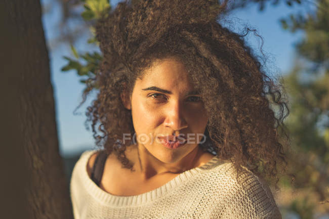 Retrato de mulher iluminada pelo sol em suéter branco olhando para a câmera na natureza — Fotografia de Stock