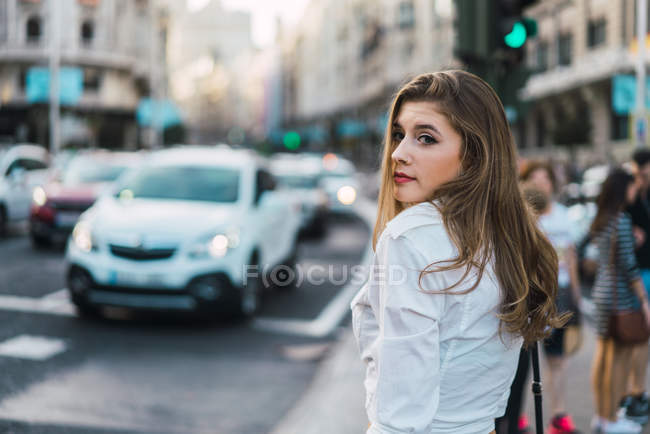 Elegante donna in posa sul marciapiede e guardando oltre la spalla alla fotocamera — Foto stock
