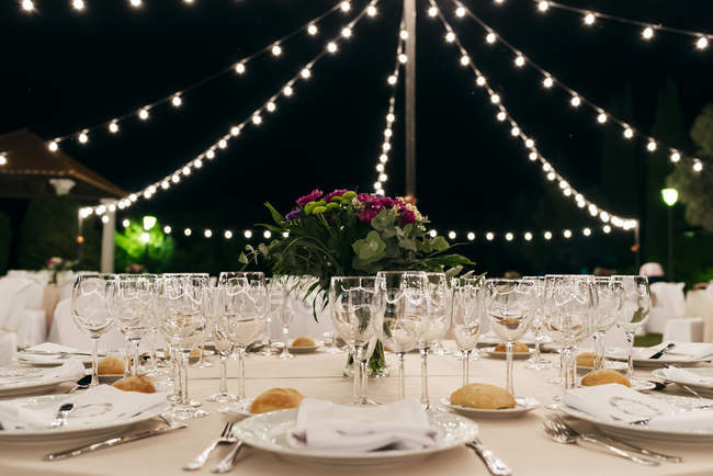 Vista de perto da mesa do banquete sob pequenas luzes à noite . — Fotografia de Stock