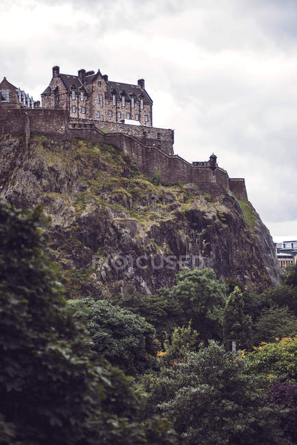 Castillo oscuro de Edimburgo de pie sobre roca musgosa sobre el cielo nublado - foto de stock