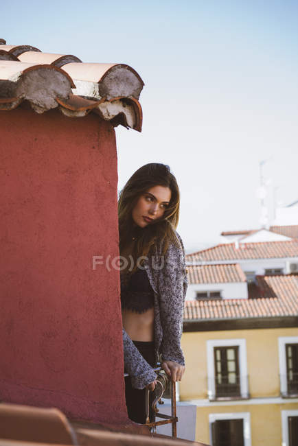 Portrait de fille brune en haut et cardigan posant sur le balcon sur les toits de la ville — Photo de stock