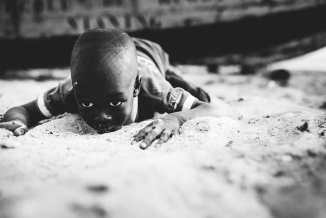 Yoff, Senegal - December 6, 2017: Portrait of African boy lying on sand — стоковое фото