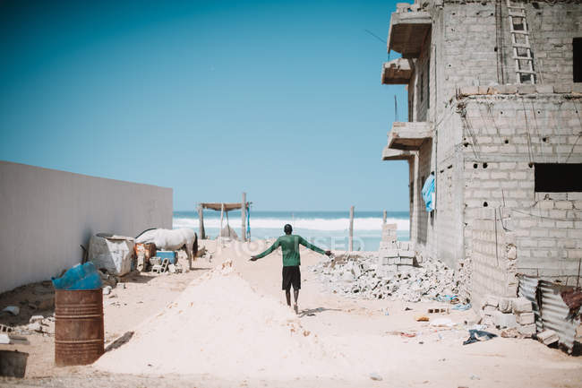 Back view of man walking on sandy construction site with grungy exterior on background of ocean. — Stock Photo