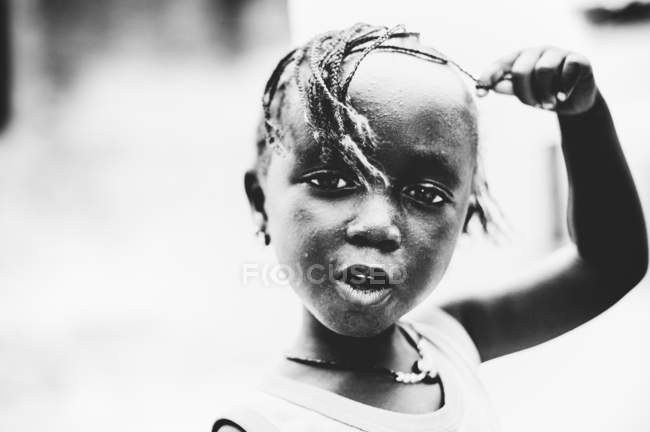 Goree, senegal- 6. Dezember 2017: Porträt eines süßen afrikanischen Mädchens, das mit Haaren spielt und in die Kamera blickt. — Stockfoto