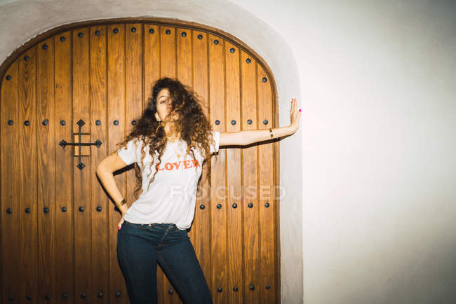 Portrait of curly woman in casual outfit posing in old doorway and looking at camera. — Stock Photo