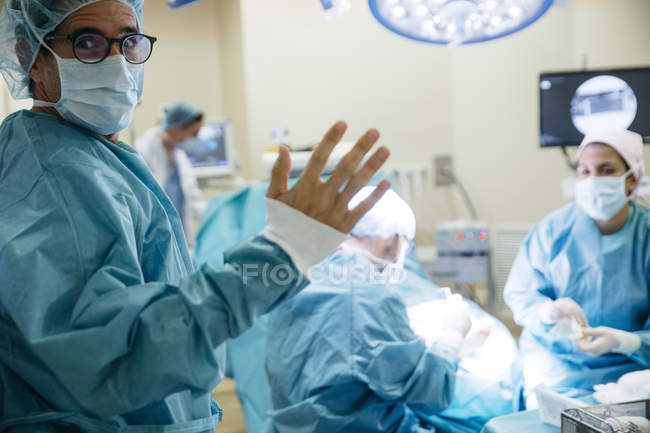 Вид через окно на хирурга в форме жеста с рукой на камеру — стоковое фото