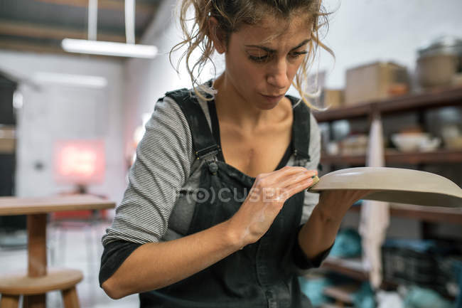 Retrato de alfarero humedeciendo plato de arcilla en taller - foto de stock