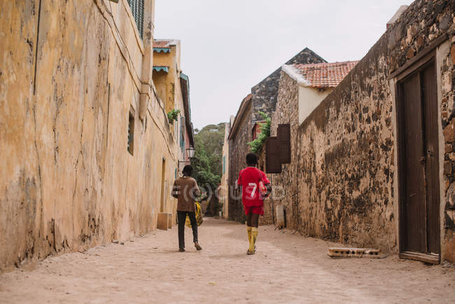 Goree, Senegal - 6 de diciembre de 2017: Vista trasera de dos chicos africanos caminando por la calle en una pequeña ciudad africana . - foto de stock