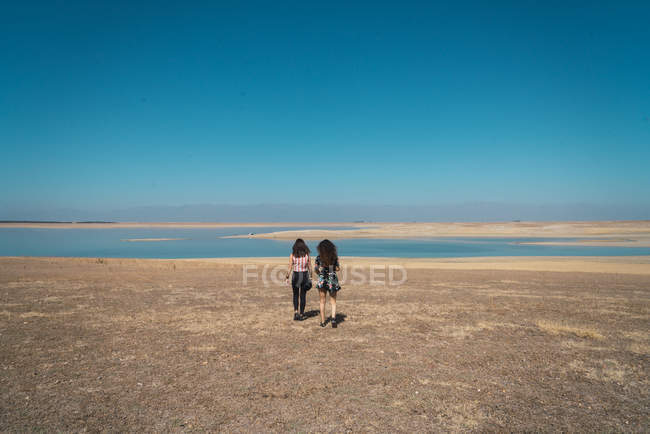 Vue arrière des femmes marchant sur un paysage plat sablonneux avec lac — Photo de stock