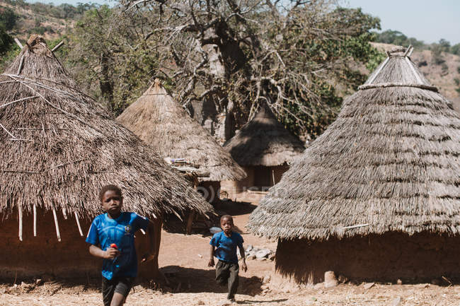 Goree, Senegal - 6 de diciembre de 2017: Niños corriendo entre bungalows en pueblo nativo a la luz del sol . - foto de stock