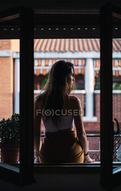 Rear view of brunette girl sitting on windowsill at balcony — Stock Photo