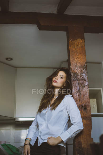 Sensual menina morena em roupas casuais inclinando-se no pilão de madeira e olhando para a câmera . — Fotografia de Stock