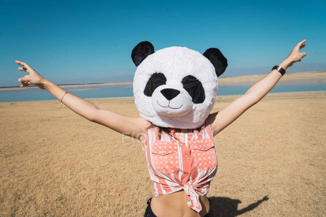 Donna con panda testa giocattolo in posa sulla riva del lago deserto con le mani tese — Foto stock
