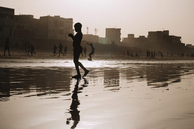 Yoff, Сенегалу - 6 грудня 2017: силует дитини, що відображають у мілкій воді поверхні на фоні, вулиця сцени в серпанок сонячного світла. — стокове фото