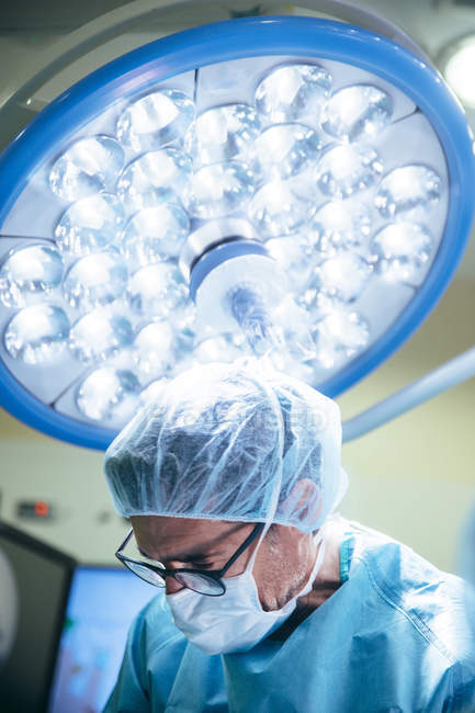 Портрет хирурга в маске, смотрящего вниз на фоне лампы — стоковое фото