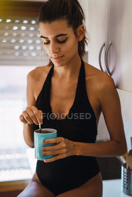 Brunette girl in swimsuit drinking coffee in kitchen — Stock Photo