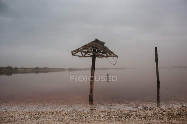 Вид на пошкоджену солом'яну парасольку, що стоїть на порожньому пляжі — стокове фото