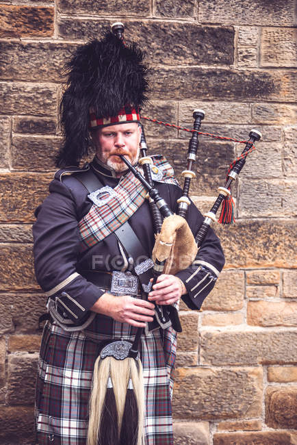 EDINBURGH, SCOTLAND - AUGUST 27, 2017: Man in traditional Scottish costume playing bagpipe on brick wall background. — Stock Photo