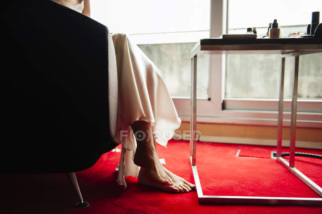 Section basse de la femme en robe de nuit en soie assise à la table dans la chambre — Photo de stock