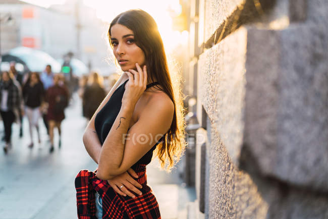 Vista laterale di sottile ragazza bruna in posa in strada illuminata dal sole e guardando la fotocamera — Foto stock