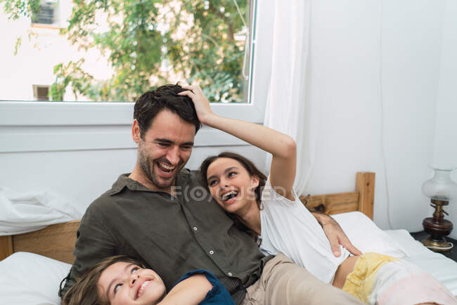 Смеющийся мужчина с детьми в постели — стоковое фото