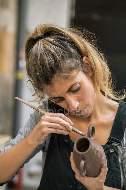 Confident woman glazing clay pot with brush — Stock Photo