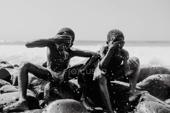 Goree, senegal- 6. Dezember 2017: fröhliche schwarze Kinder waschen Gesichter auf Felsen in Wellen — Stockfoto