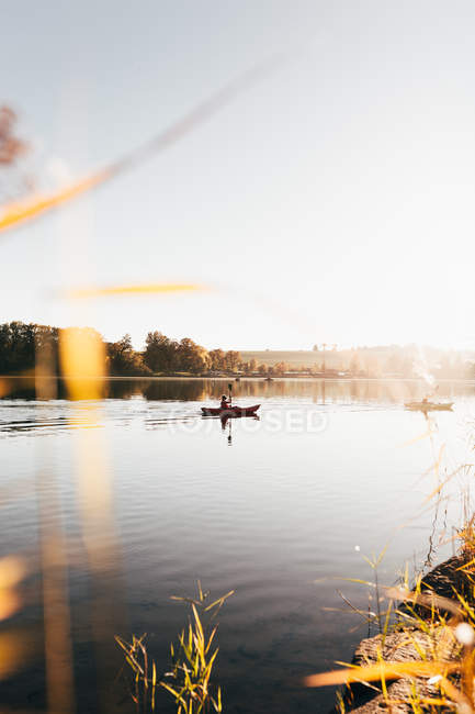 Landscape of tranquil lake water in morning haze with travelers rowing in kayaks. — Stock Photo