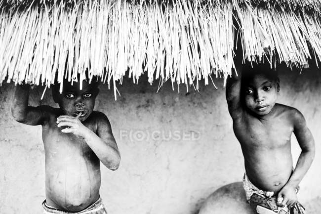 Kedougou, Sénégal- 6 décembre 2017 : Deux garçons debout sous le toit de paille du bungalow et regardant la caméra — Photo de stock