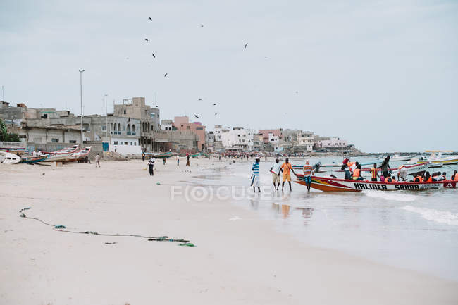 Goree, Senegal- 6 de dezembro de 2017: Vista lateral do povo africano em pé no navio na costa arenosa em dia ensolarado . — Fotografia de Stock