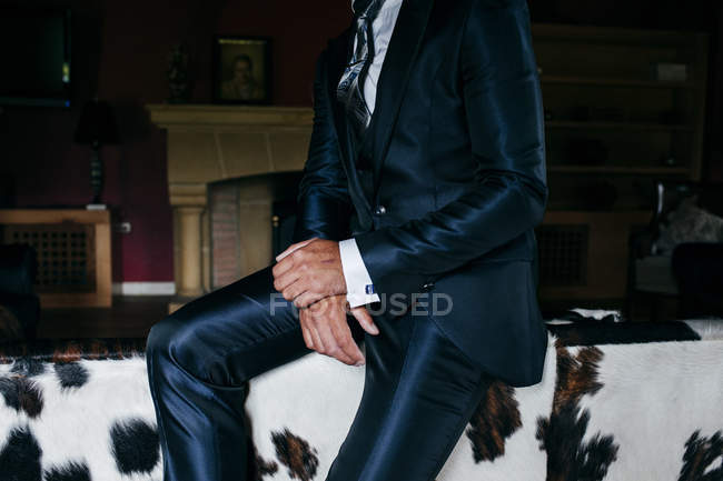 Crop elegant man in shiny dark blue suit sitting on coach back — Stock Photo