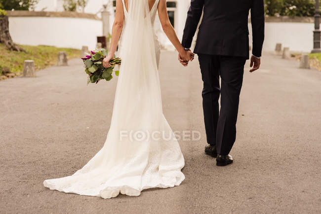Crop bride and groom holding hands and walking on street — Stock Photo