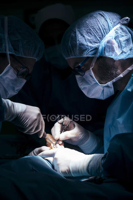 Vista lateral de dos cirujanos operando paciente en luz de lámpara - foto de stock
