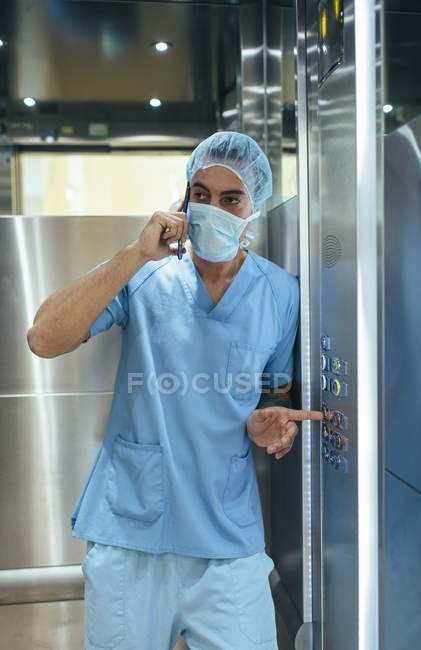Людина в погонах лікар стояв у лікарняного ліфта і говорити на смартфоні. — стокове фото