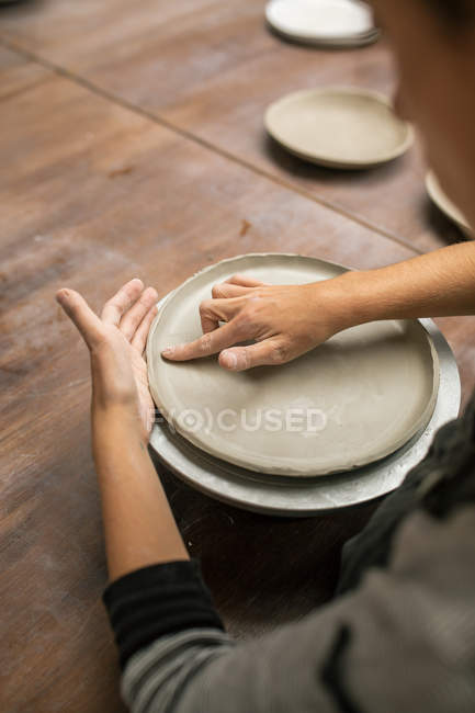 Sopra vista di spalla di vasaio che forma il piatto da argilla a desktop — Foto stock
