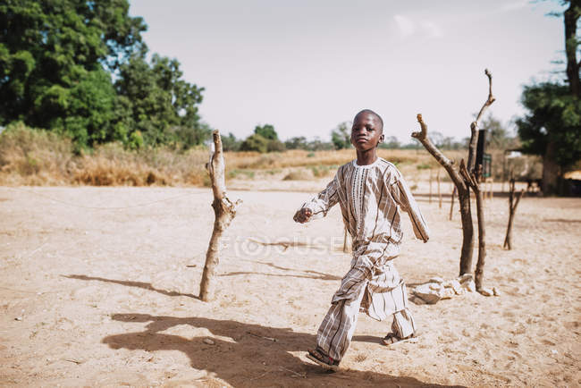Goree, Senegal- 6 de dezembro de 2017: Menino andando na areia na área rural e olhando para a câmera com confiança . — Fotografia de Stock